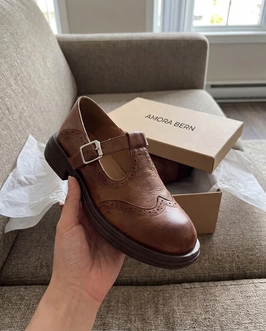 Brauner T-Steg-Schuh in der Hand neben der AMORA BERN-Schachtel