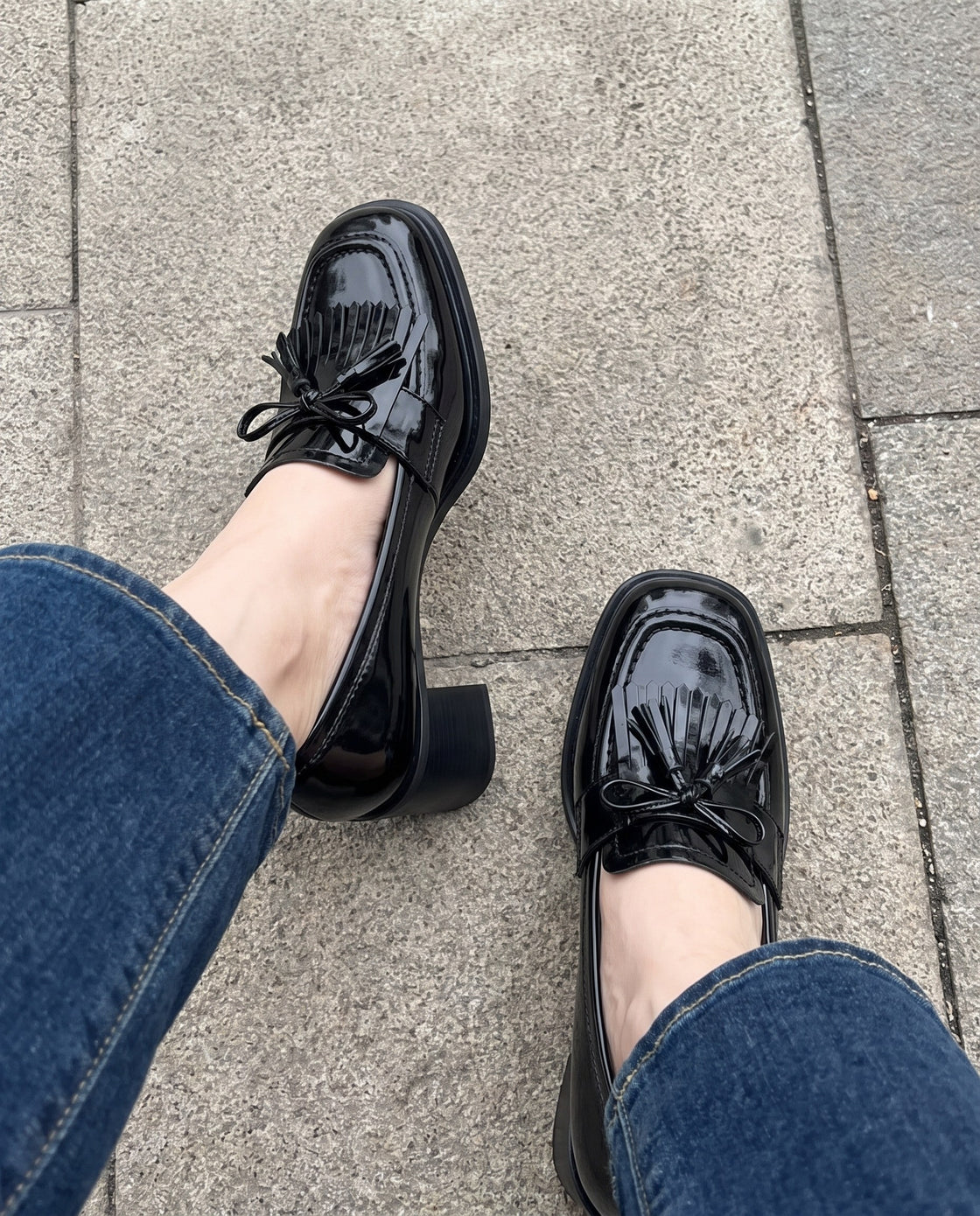 Schwarze Lack-Loafer mit Fransen zu einer Jeans auf dem Gehsteig